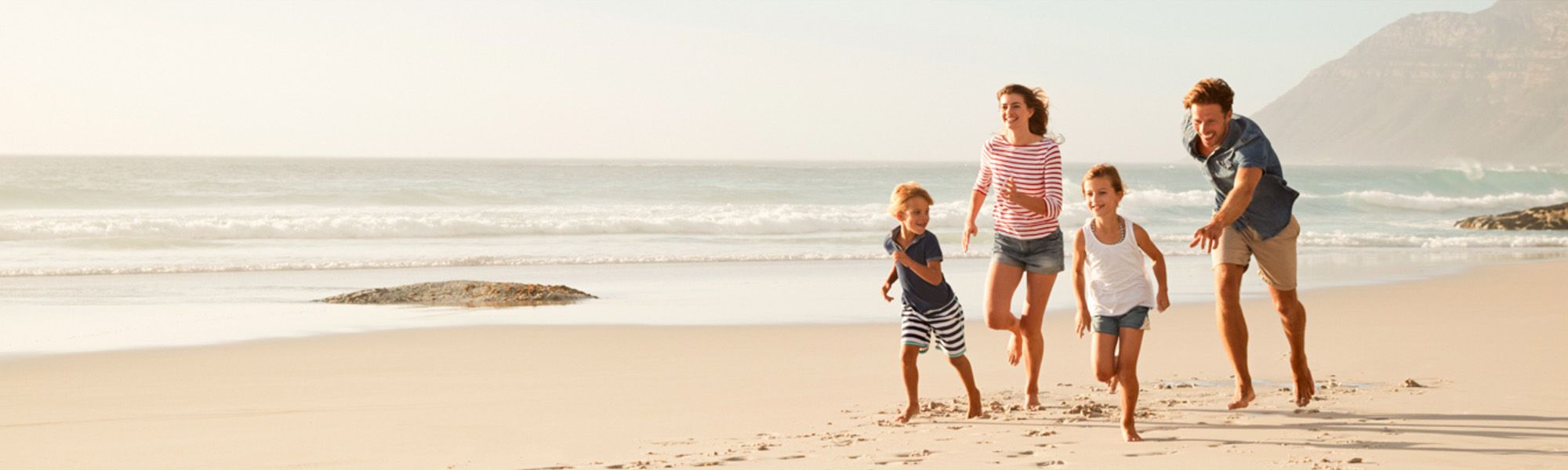 Ein Mann, eine Frau, ein kleiner Junge und ein kleines Mädchen spielen am Strand und toben am Wasser gemeinsam. Es ist Sommer, dass Meer ruhig und es scheint die Sonne.