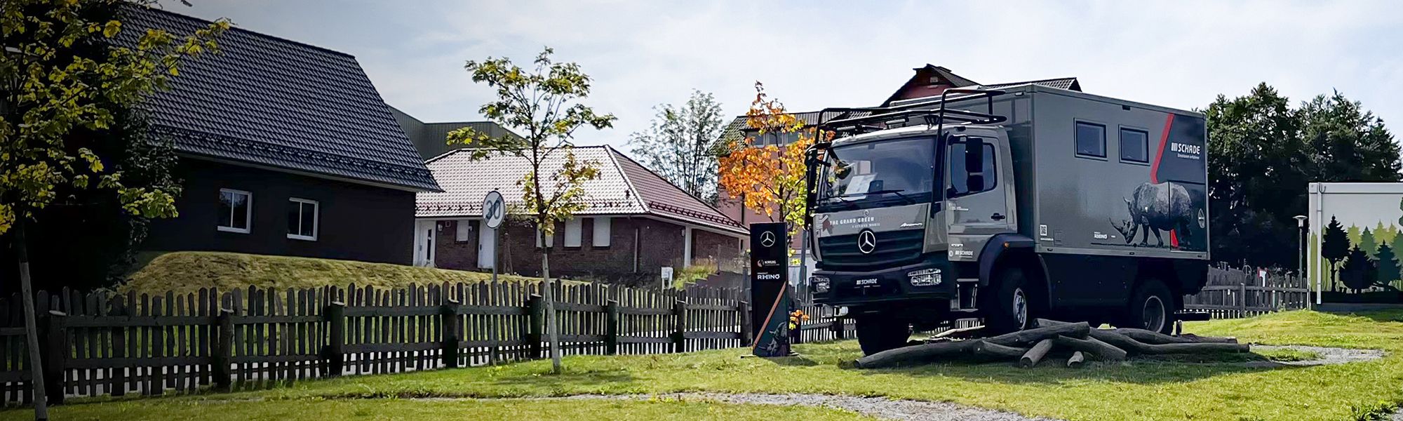 Projekt RHINO Kurg Expiditionsmodell in Oberhof am Grand Green Hotel. Das Fahrzeug steht auf der Wiese. Ein Holzzaun sowie Häuser sind im Hintergund zu sehen. Baumstämme liegen vor dem Rhino.