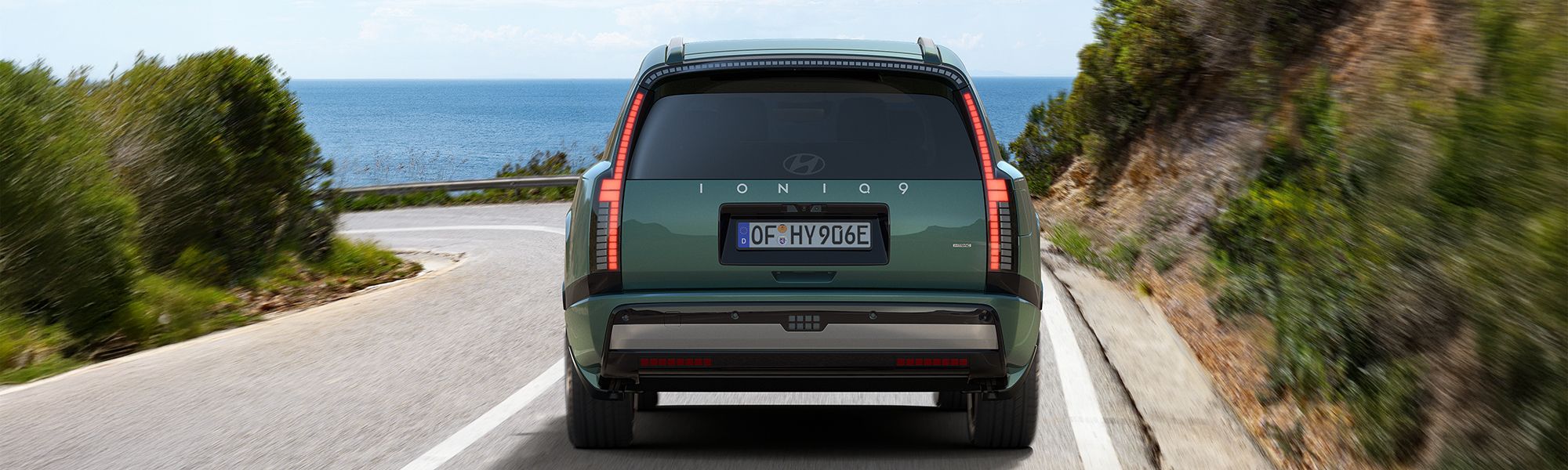 Hyundai IONIQ 9 ionosphere green, fährt auf einer Straße an der Steilküste entlang. Das Fahrzeug wird von hinten gezeigt. 