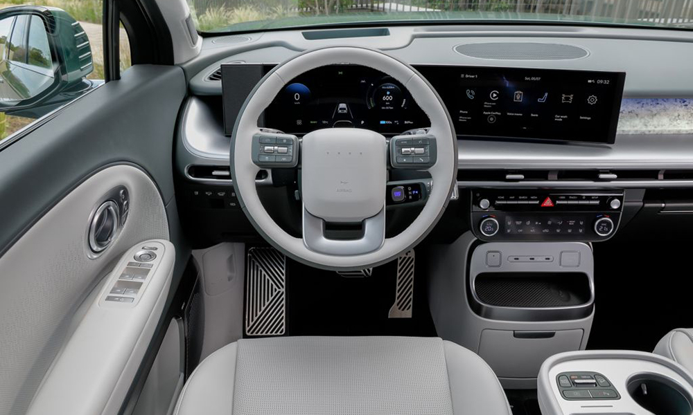 Hyundai IONIQ 9. Vom Fahrersitz aus ist das Cockpit mit hellgrauen Lenkrad und das durchgezogene leicht geschwungene Display fotografiert.