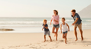 Hier kommen Sie zur SCHADE Sommeraktion. Ein Mann, eine Frau, ein kleiner Junge und ein kleines Mädchen spielen am Strand und toben am Wasser gemeinsam. Es ist Sommer, dass Meer ruhig und es scheint die Sonne.