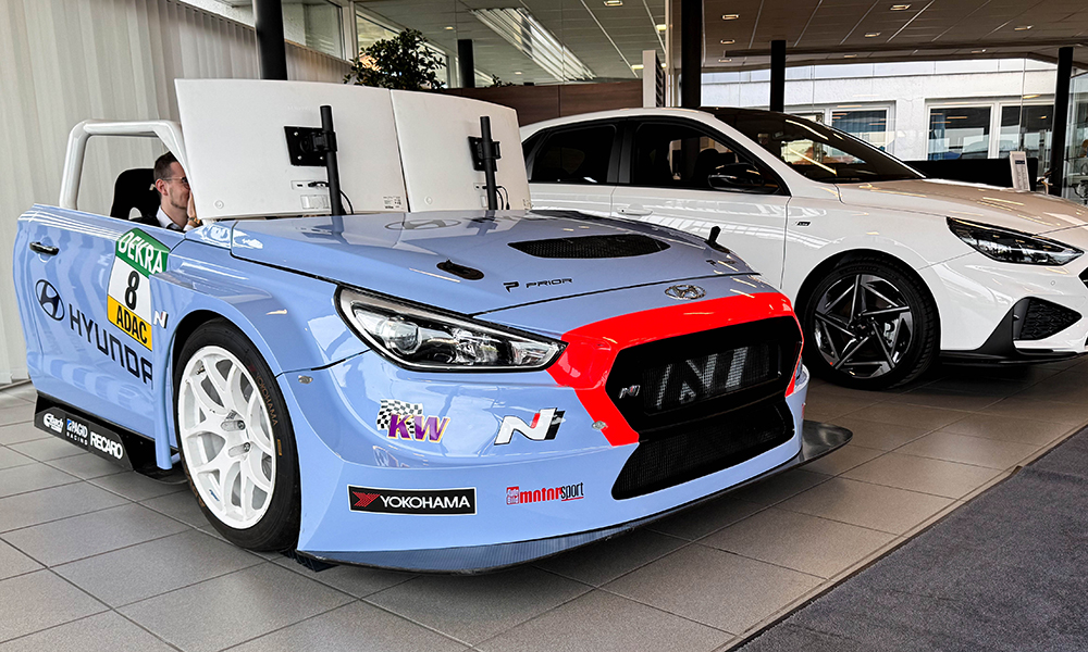 Blauer Hyundai Fahrsimulator in Ausstellungshalle neben weißem Hyundai Fahrzeug